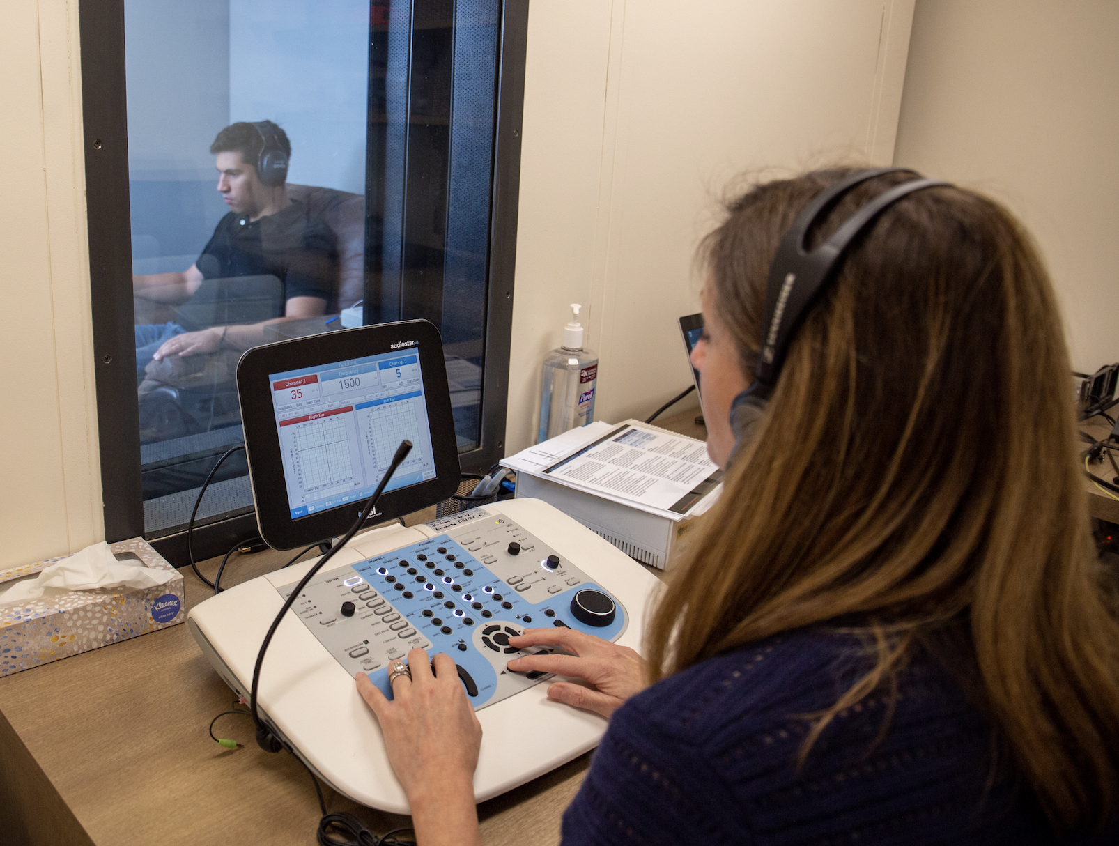 KB at an audiometer testing a young man's hearing